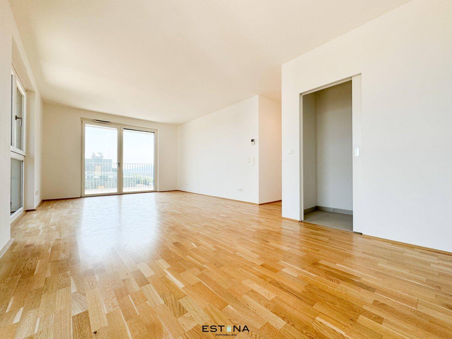 Geräumiges, leeres Zimmer mit Holzboden, Balkonzugang und offenem Durchgang.