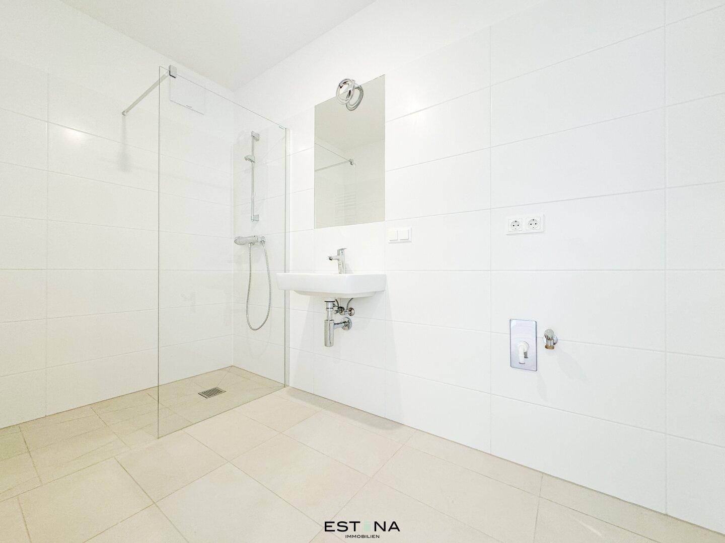 Modernes Badezimmer mit weißen Fliesen, einer begehbaren Dusche und einem einzelnen Waschbecken.