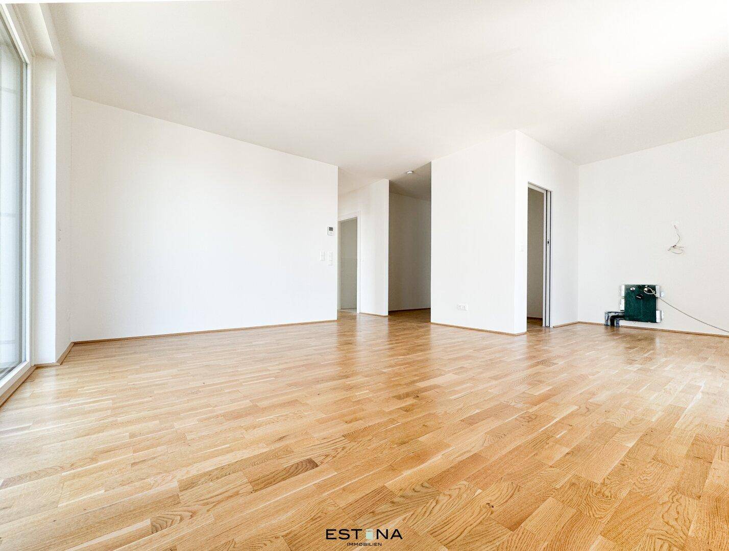 Heller, leerer Raum mit Holzboden und vorbereiteten Anschlüssen für eine Küche.