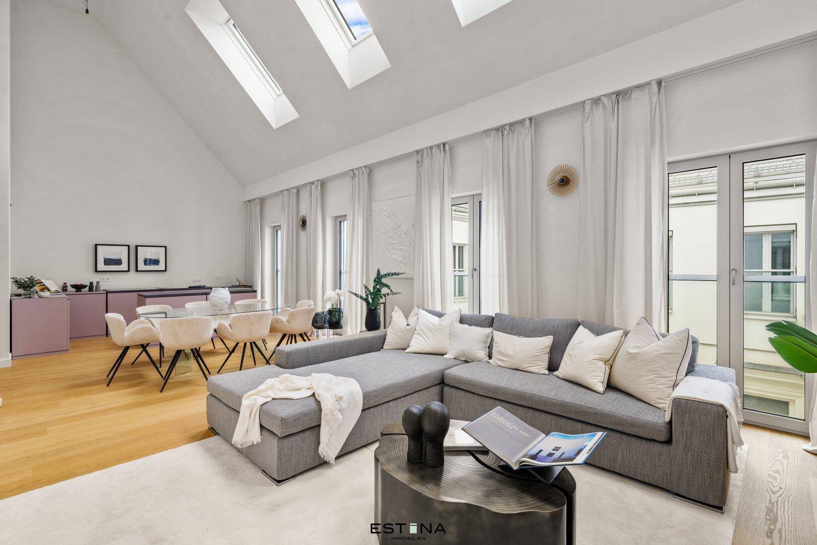 Geräumiger Wohnbereich mit bequemer Couch, Holzboden und viel Tageslicht durch große Fenster und Dachfenster.