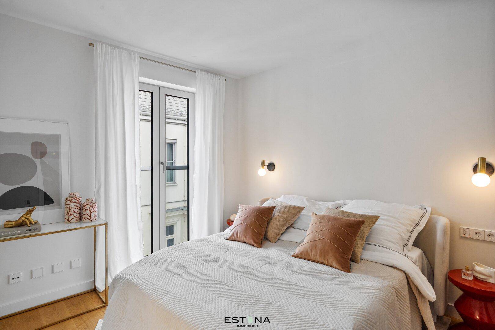 Helles Schlafzimmer mit Doppelbett, Holzboden und Zugang zu einem französischen Balkon.