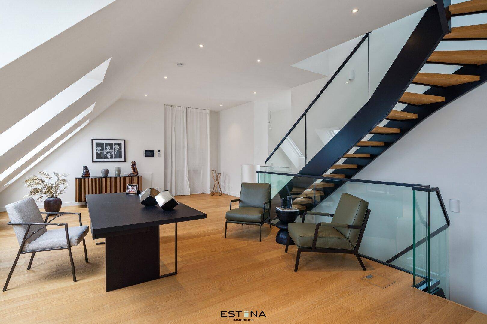 Stilvoller Arbeitsbereich mit Holzboden, schräger Decke und moderner Treppe mit Glasgeländer.