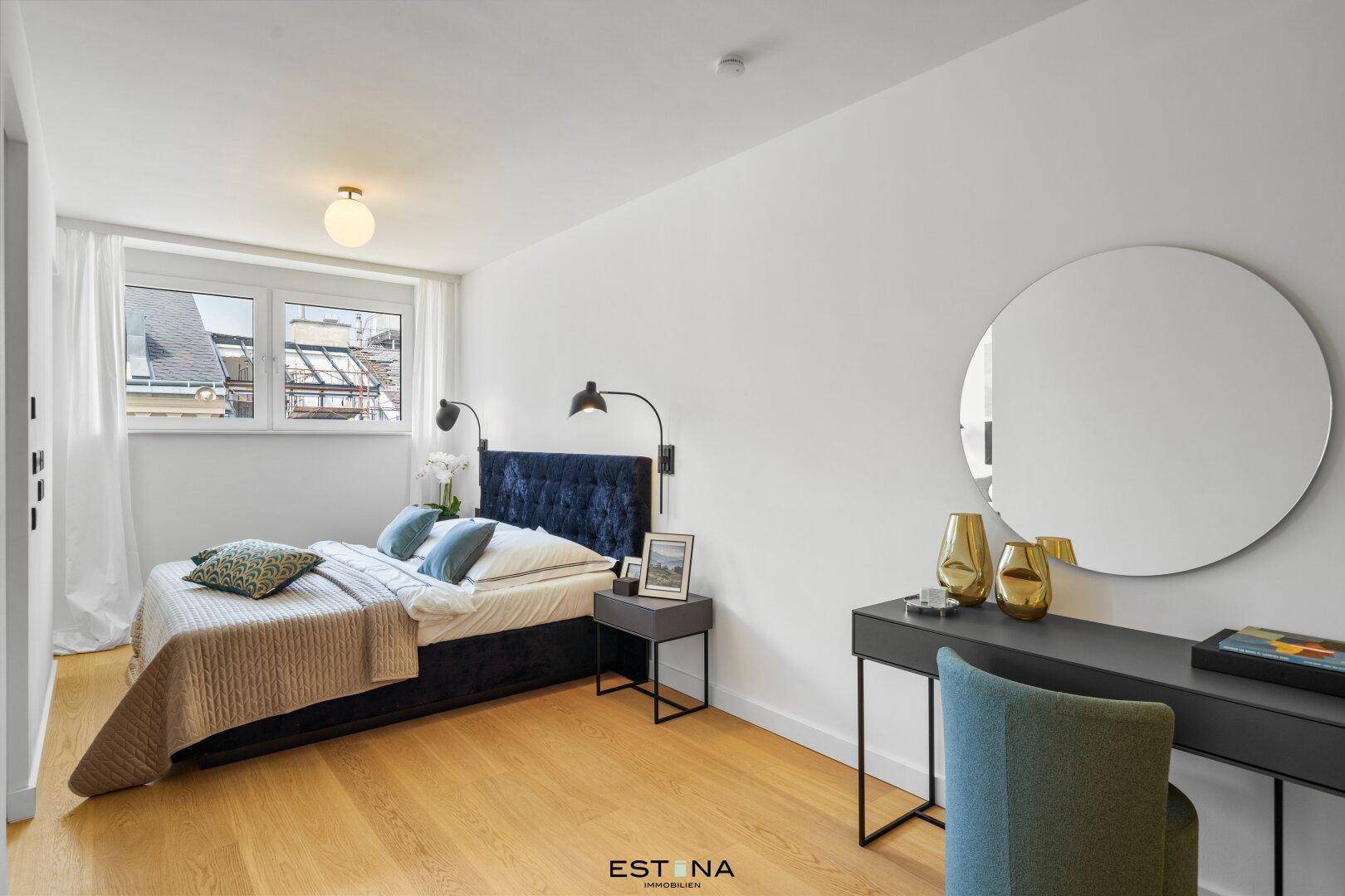 Gemütliches Schlafzimmer mit Holzboden, großem Fenster und modernem Bett mit blauer Polsterung.