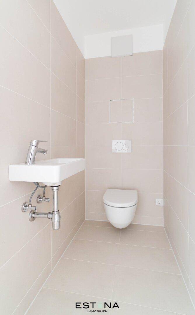 Helles Gäste-WC mit wandhängender Toilette, modernem Waschbecken und hellen Fliesen.