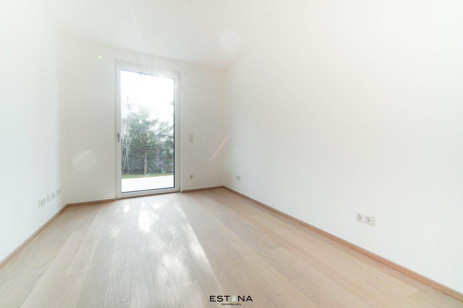 Freundliches Schlafzimmer mit hellem Parkettboden und großem Fenster mit Blick ins Grüne.