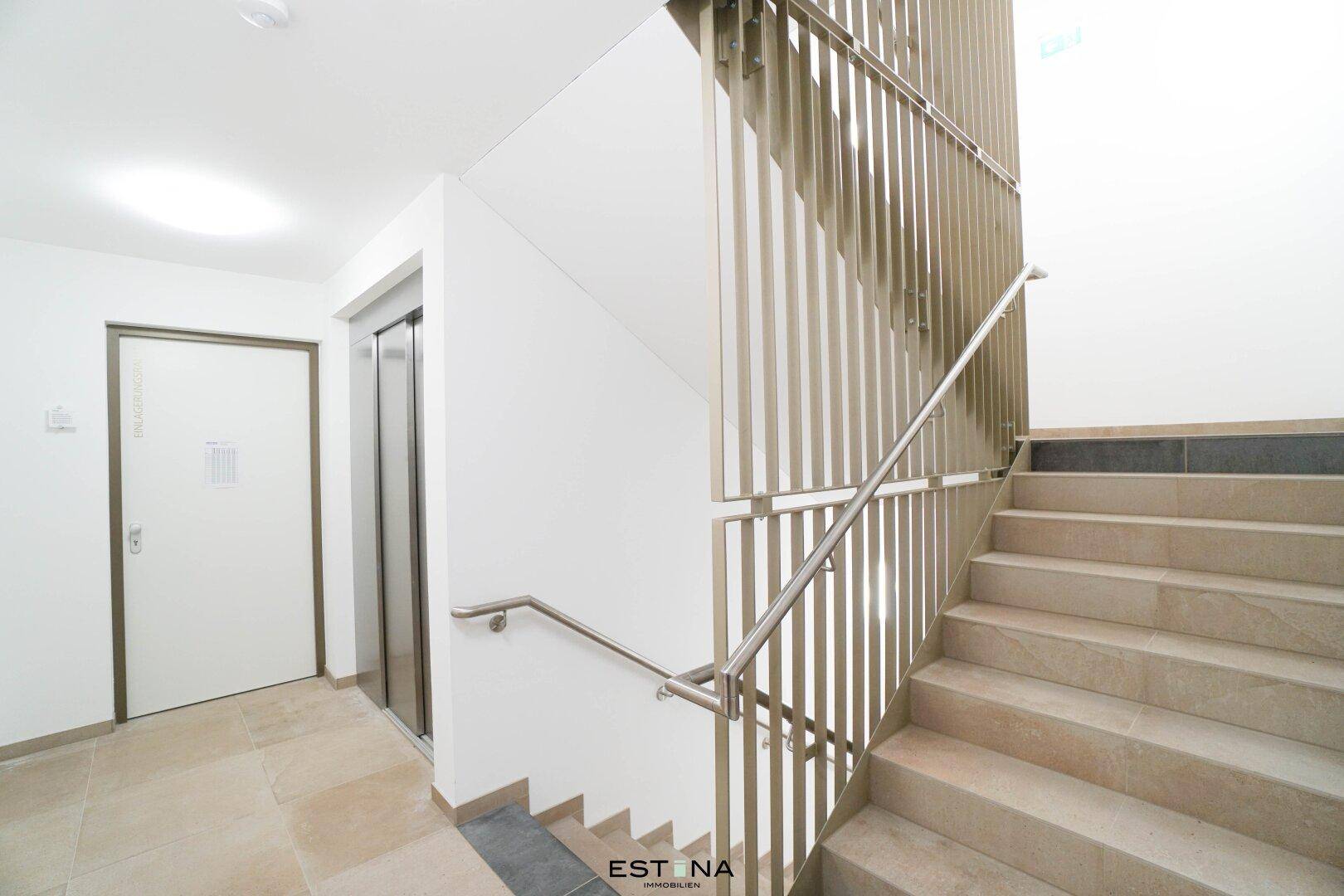 Heller Treppenaufgang mit modernem Geländer und Aufzug in einem Mehrfamilienhaus.