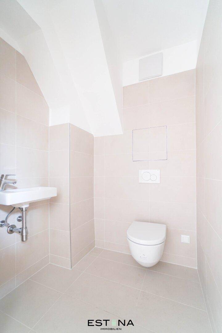 Kleines Gäste-WC mit Wand-WC, Handwaschbecken und hellen Fliesen unter Dachschräge.