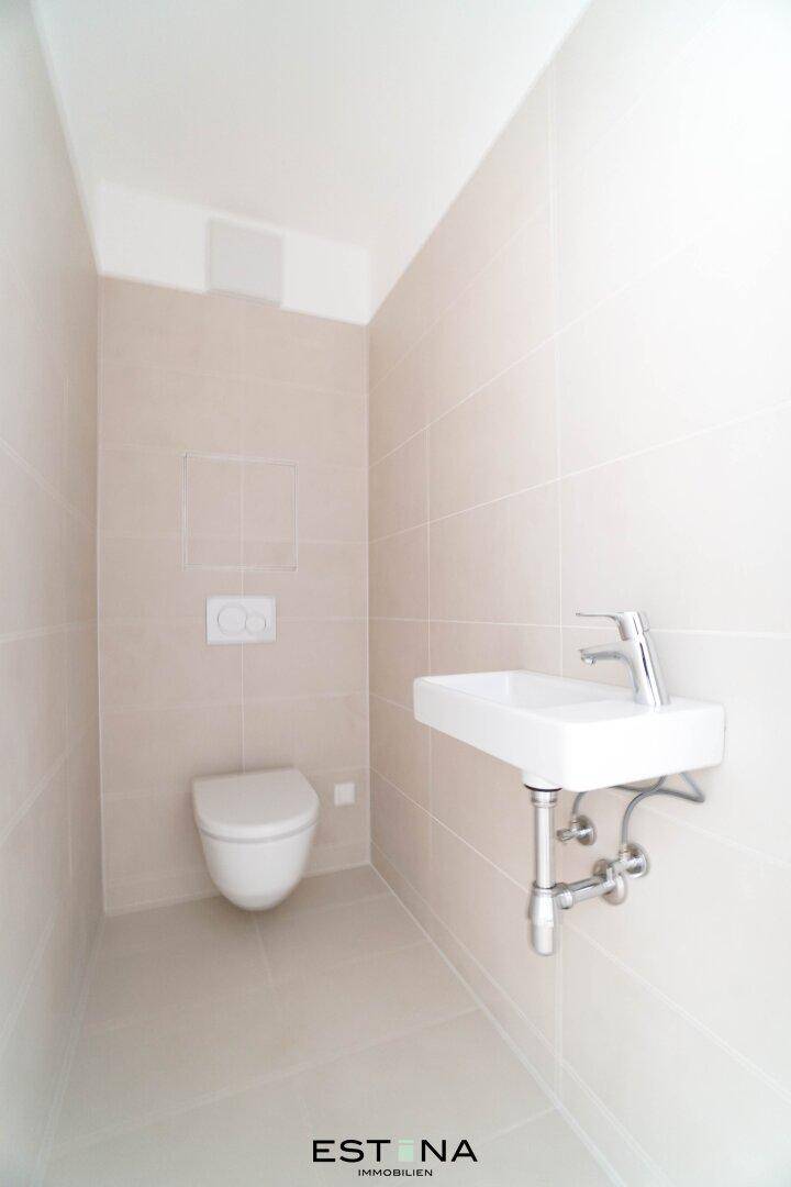 Gäste-WC mit hellen Fliesen, wandhängender Toilette und modernem Handwaschbecken.