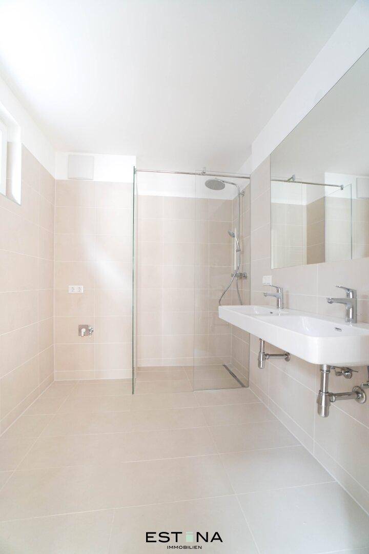 Helles Badezimmer mit großformatigen Fliesen, moderner Dusche und zwei Waschbecken.