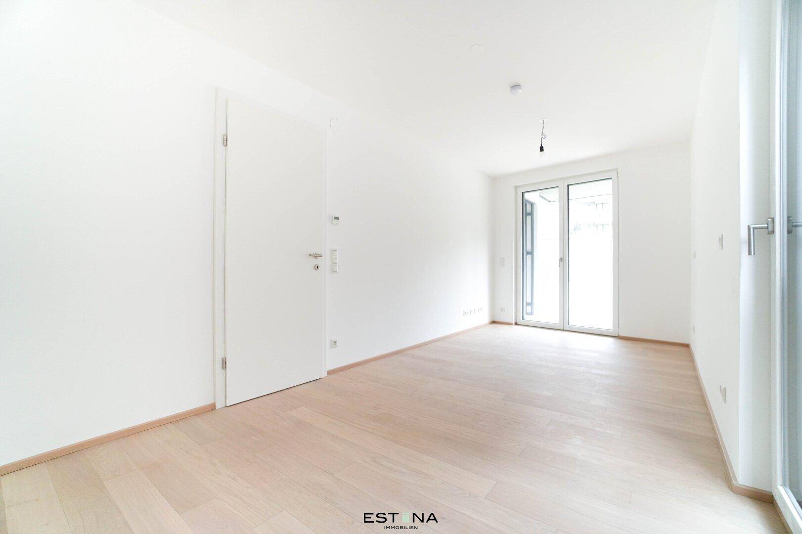 Leeres Schlafzimmer mit hellem Parkettboden und großem Fenster für viel Tageslicht.