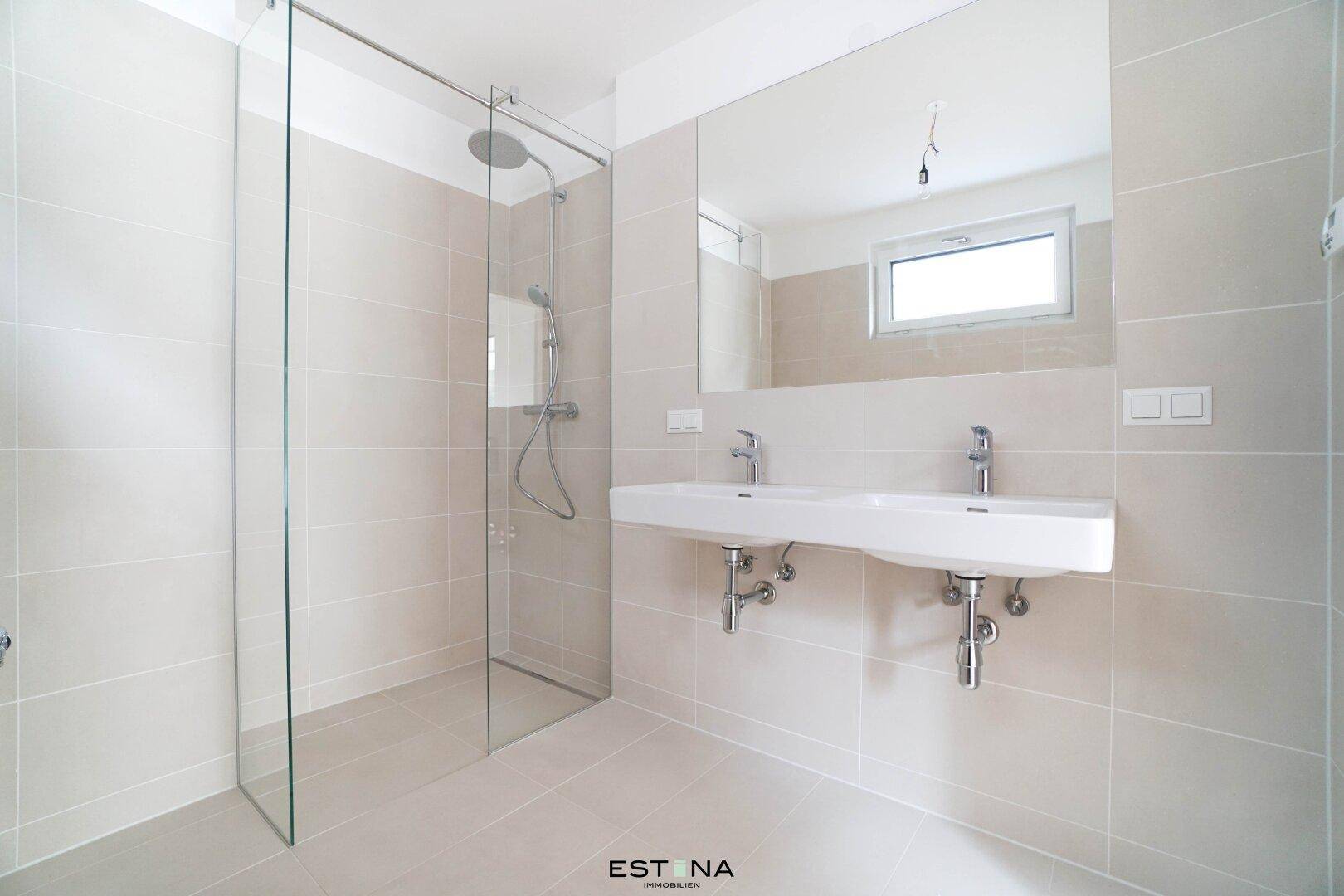 Modernes Badezimmer mit beigefarbenen Fliesen, großer begehbarer Dusche und Doppelwaschbecken.