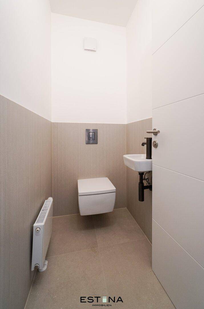 Kleines Gäste-WC mit wandhängender Toilette, kleinem Waschbecken und beigefarbenen Fliesen.