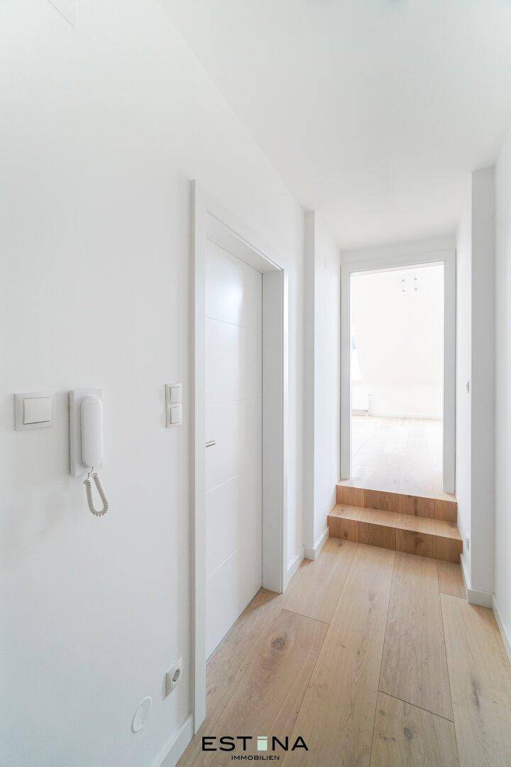 Heller Flur mit Holzfußboden, weiß gestrichenen Wänden und einer kleinen Stufe zu einem weiteren Raum.