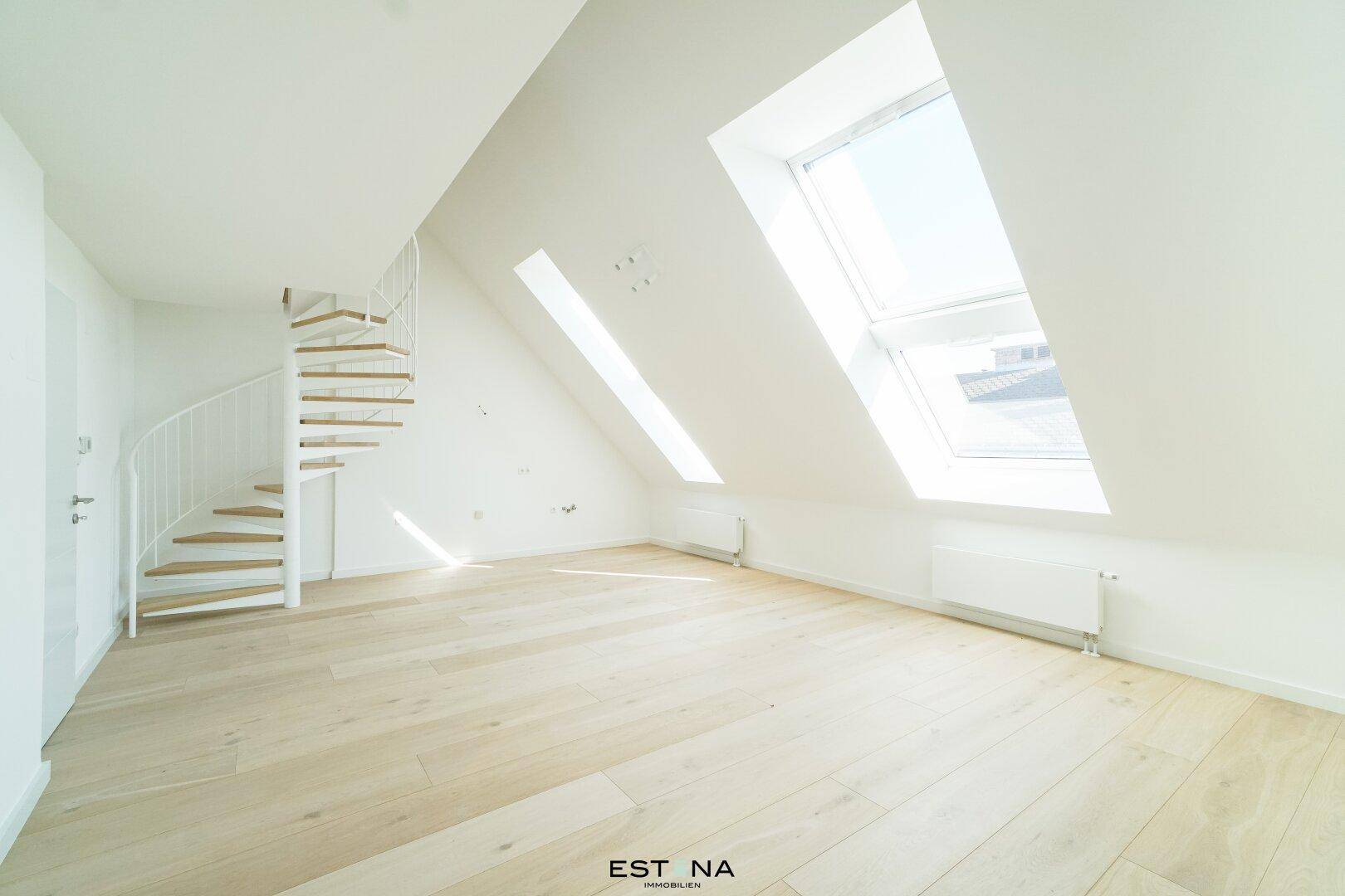 Heller, leerer Raum im Dachgeschoss mit Holzfußboden, schrägen Wänden und Wendeltreppe.