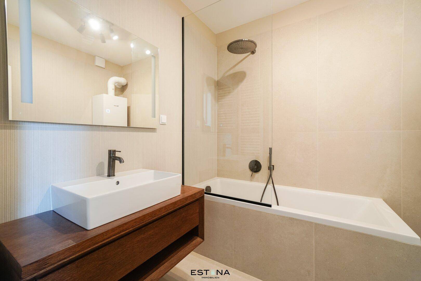 Modernes Badezimmer mit Badewanne, Duschfunktion, Einzelwaschbecken und beigefarbenen Fliesen.