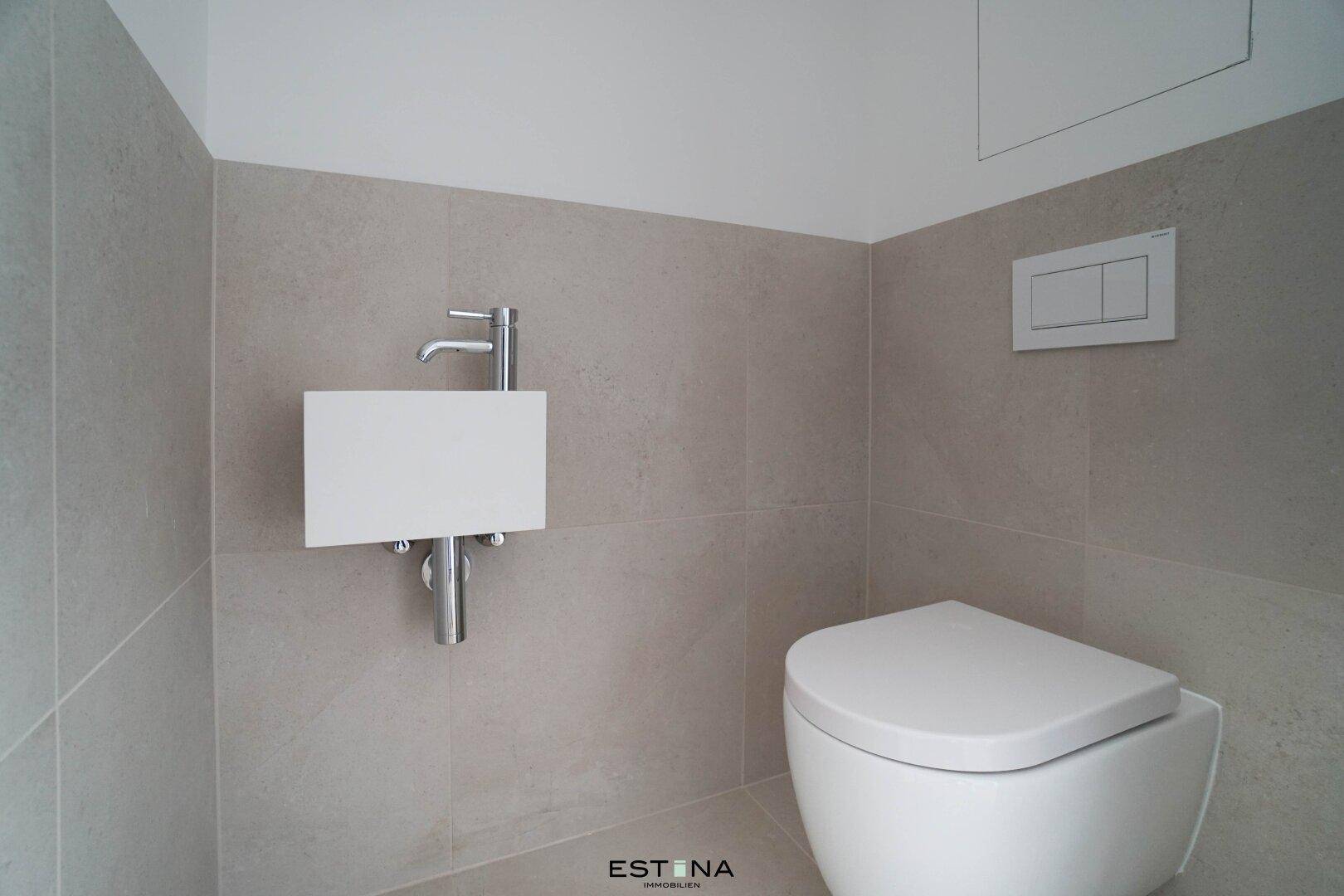 Modernes WC mit Wandtoilette und kleinem Waschbecken, in neutralen Grautönen gehalten.