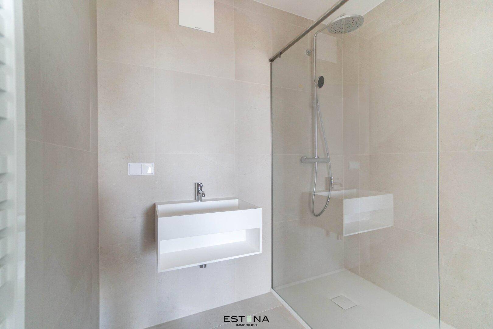 Modernes Badezimmer mit beigefarbenen Fliesen, wandhängendem Waschbecken und einer geräumigen begehbaren Dusche.