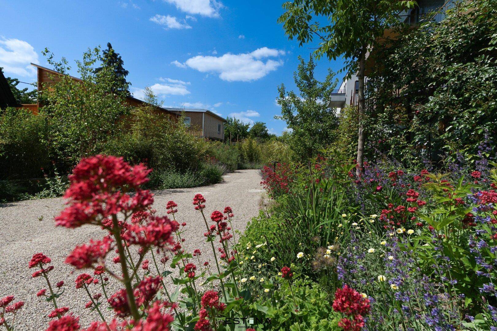 Malerischer Gartenweg, gesäumt von bunten Blumen und üppigem Grün, der zu den Gebäuden führt.