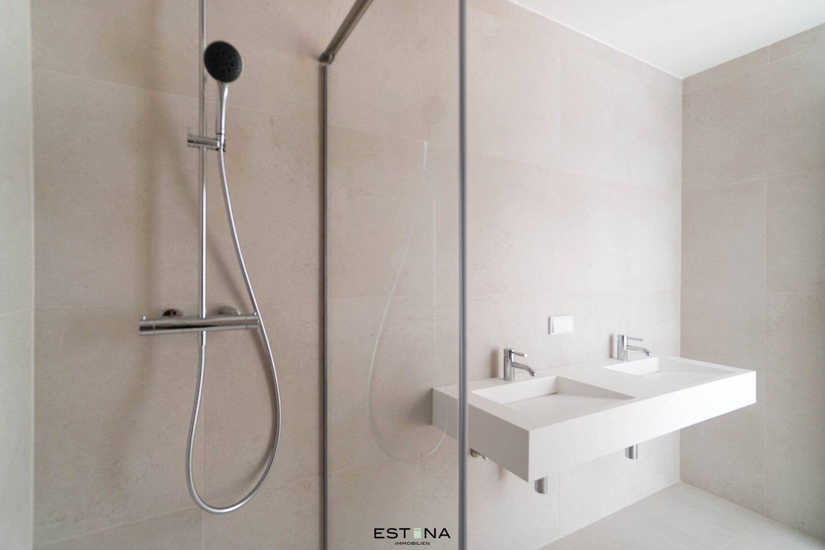 Modernes Badezimmer mit doppelten Waschbecken, großer Duschkabine und hellen Fliesen.