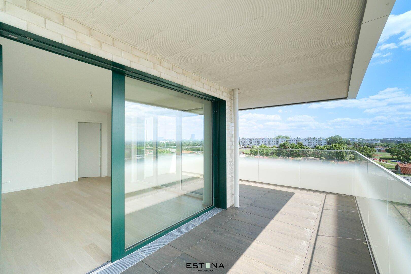 Geräumiger Balkon mit Fliesenboden und Glasgeländer, zugänglich durch eine große Schiebetür.
