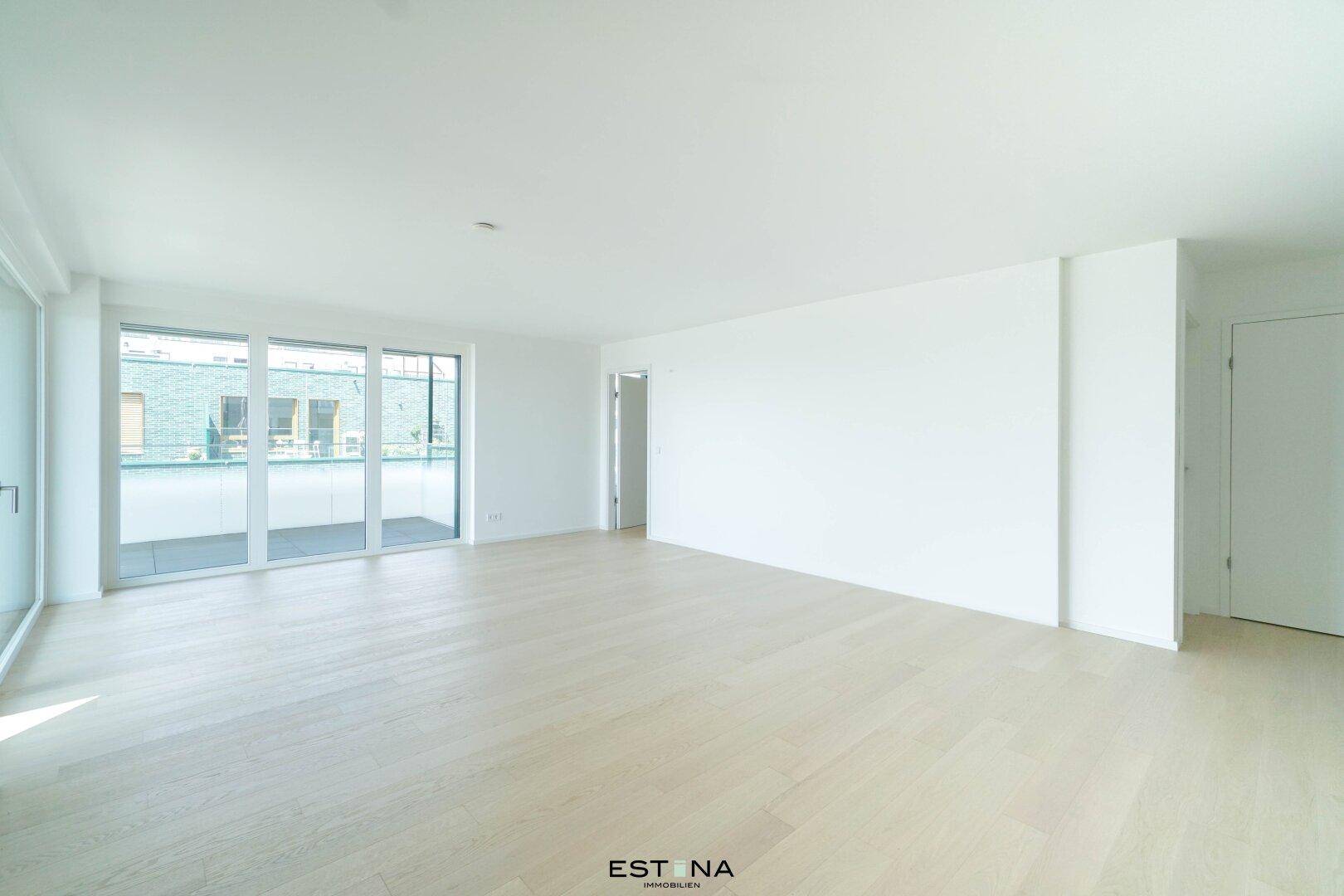 Helles, leeres Wohnzimmer mit hellem Parkettboden und Zugang zu einem großen Balkon.
