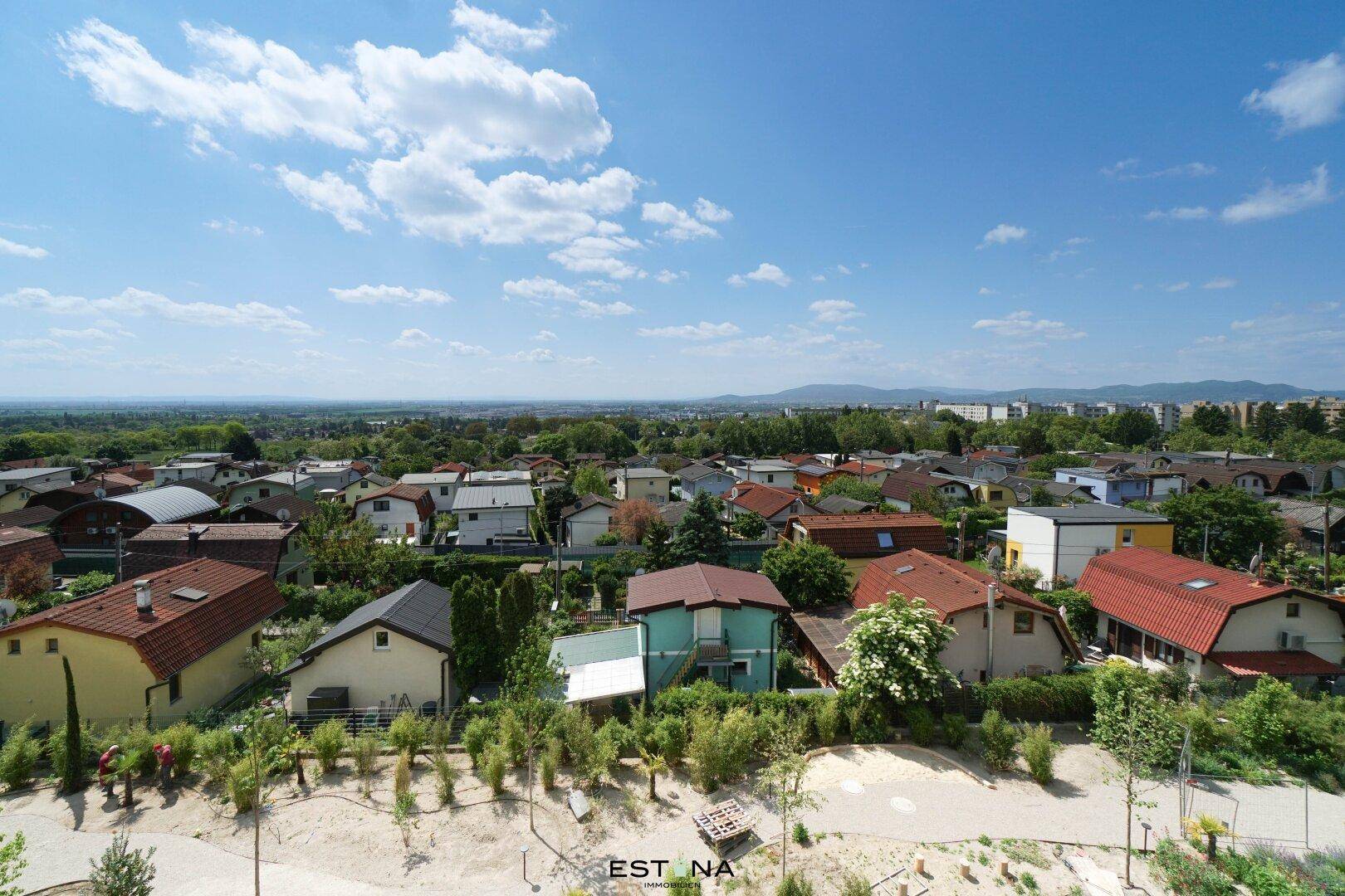 Weitläufiger Blick über eine Wohnsiedlung mit vielen Häusern und grünen Bäumen unter blauem Himmel.