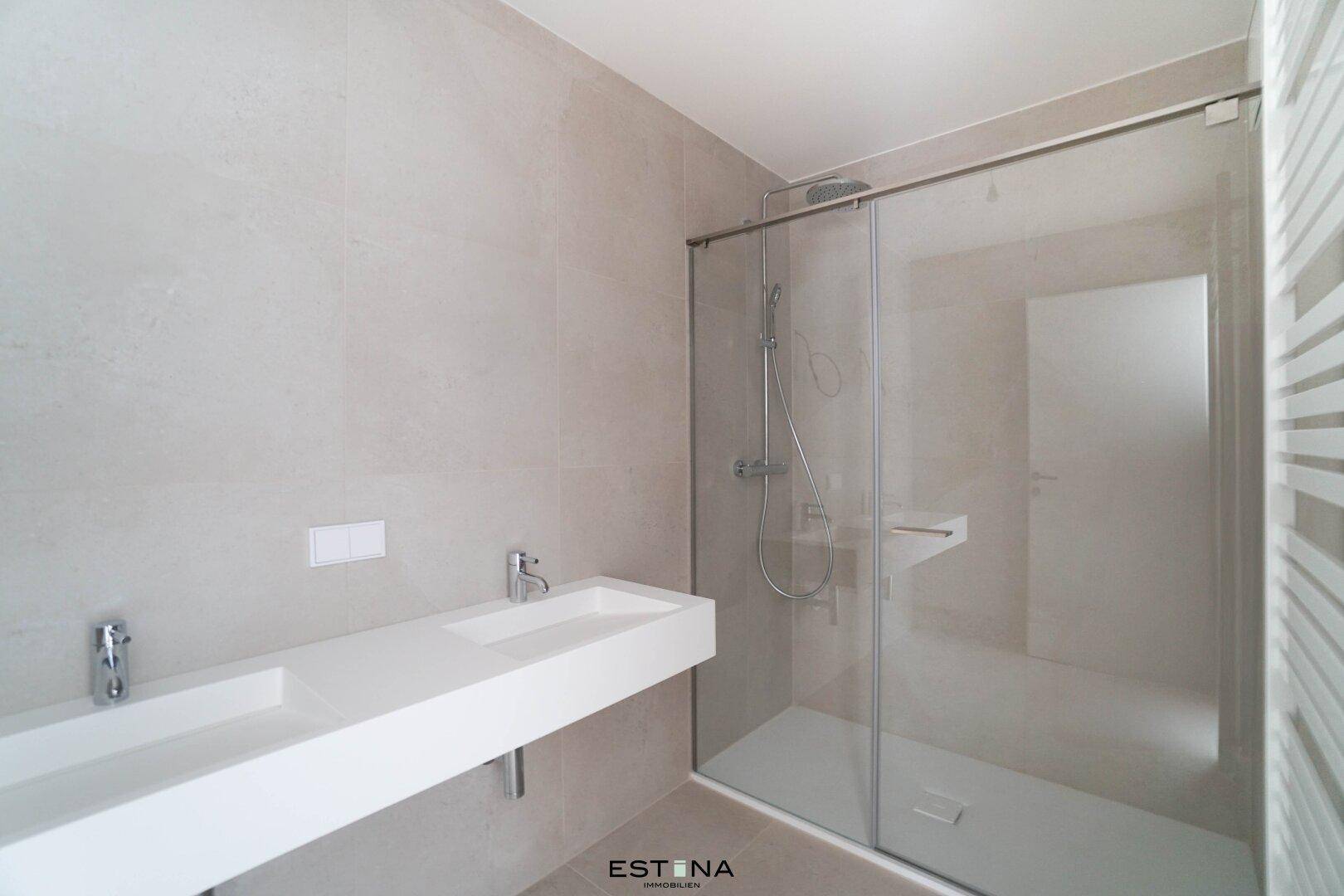 Modernes Badezimmer mit Doppelwaschbecken, großer begehbarer Dusche und hellen Fliesen.