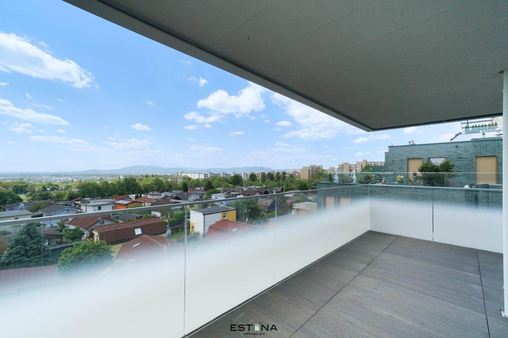 Heller Balkon mit moderner Glasbrüstung und Panoramablick auf die Stadt und die Berge.