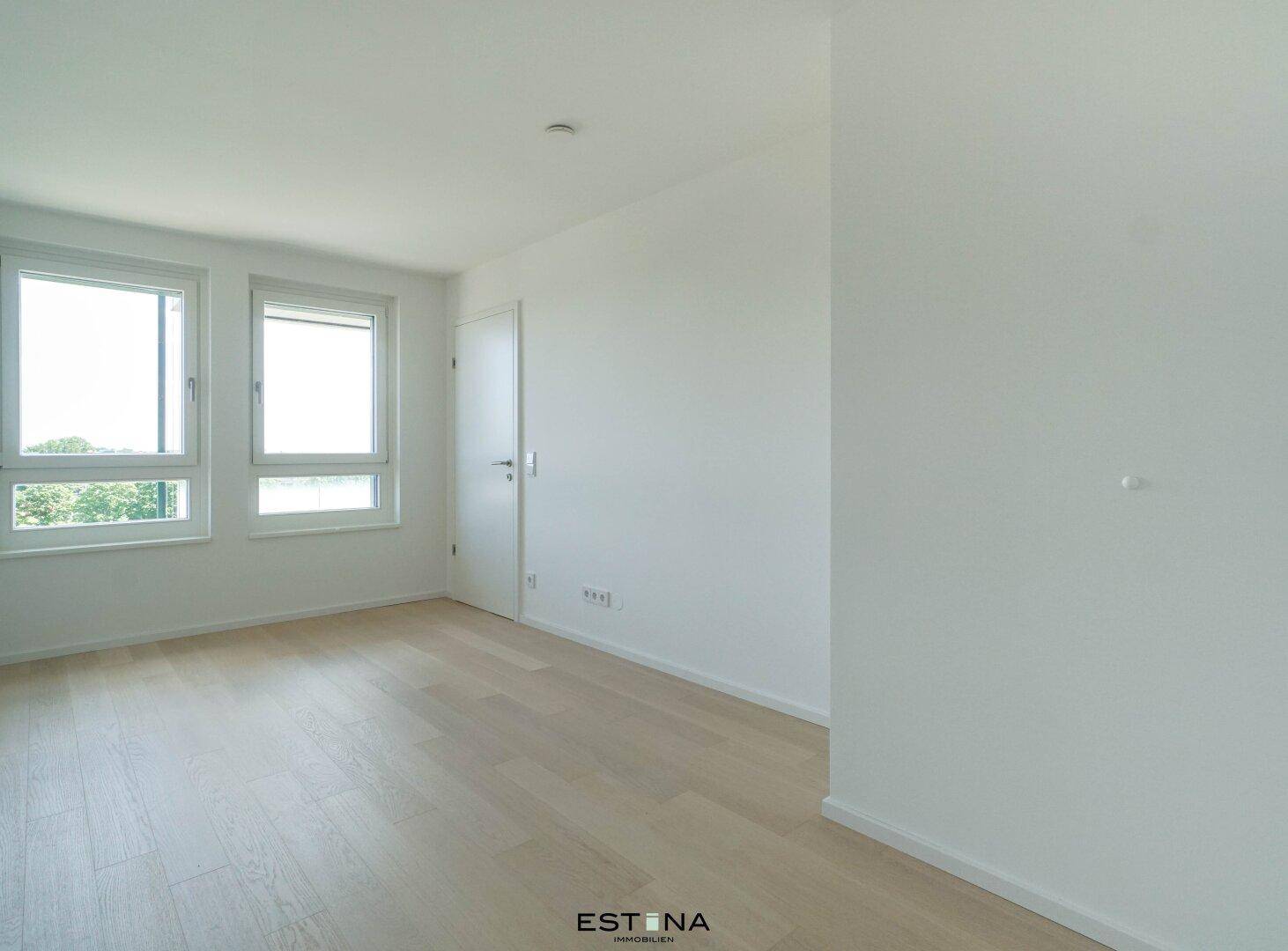 Leeres Schlafzimmer mit hellem Holzfußboden, weißen Wänden und zwei Fenstern.