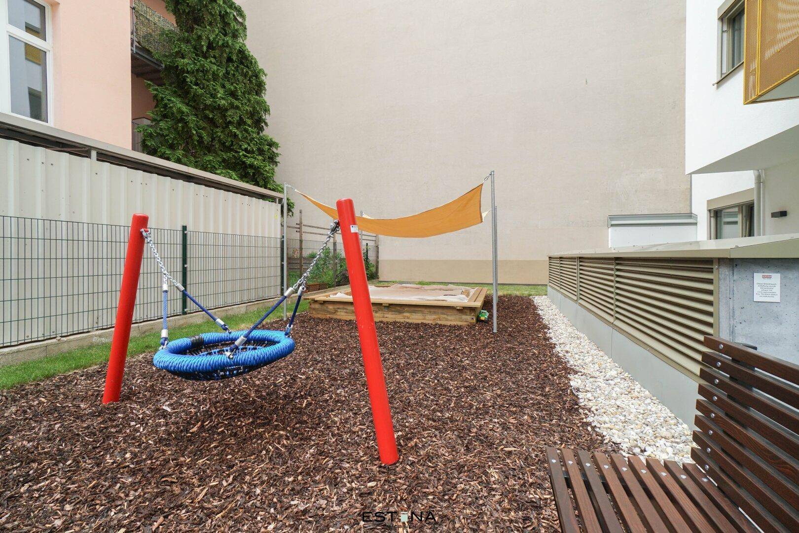 Spielplatzbereich mit Schaukel, Sandkasten und Rindenmulchboden.