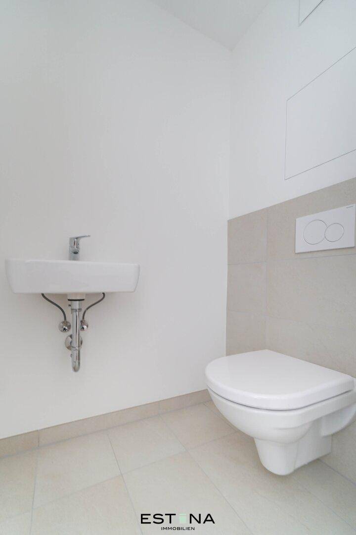 Separate Gästetoilette mit Wand-WC, kleinem Waschbecken und hellen Wandfliesen.