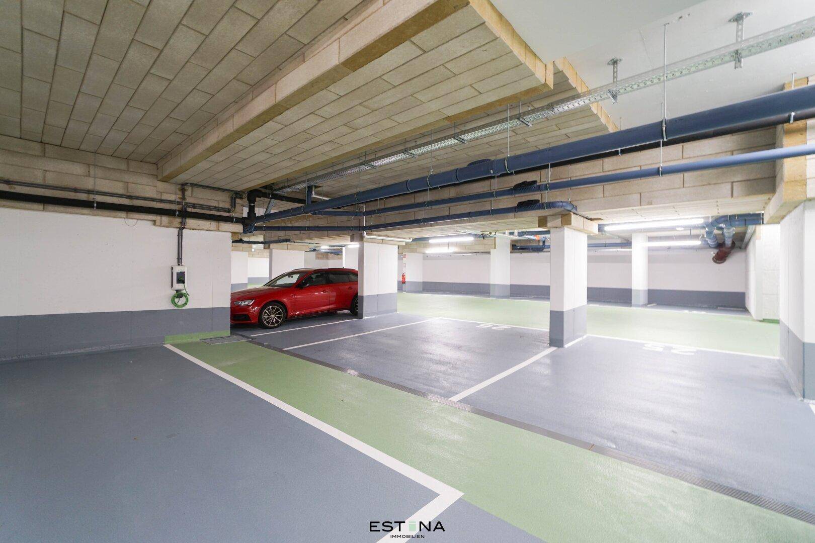 Tiefgarage mit markierten Parkplätzen und einer Ladestation für Elektrofahrzeuge.