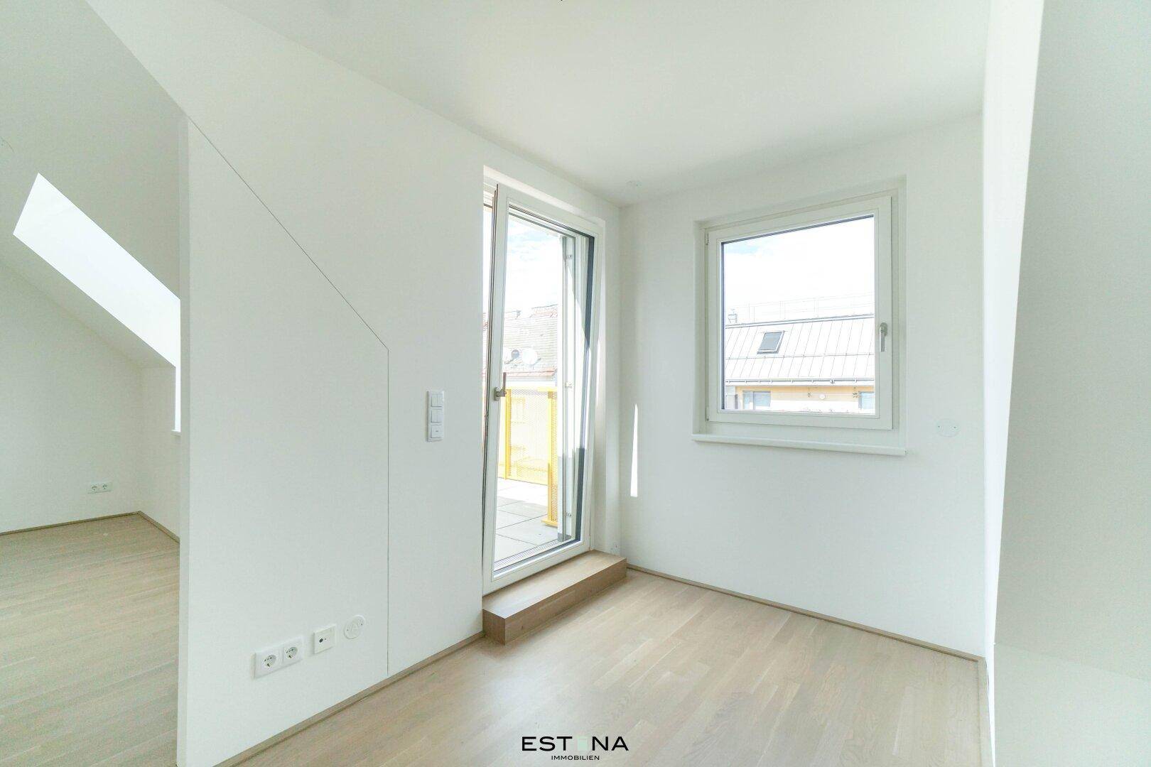 Heller Raum mit Holzboden, Fenster und Zugang zu einem Außenbereich.