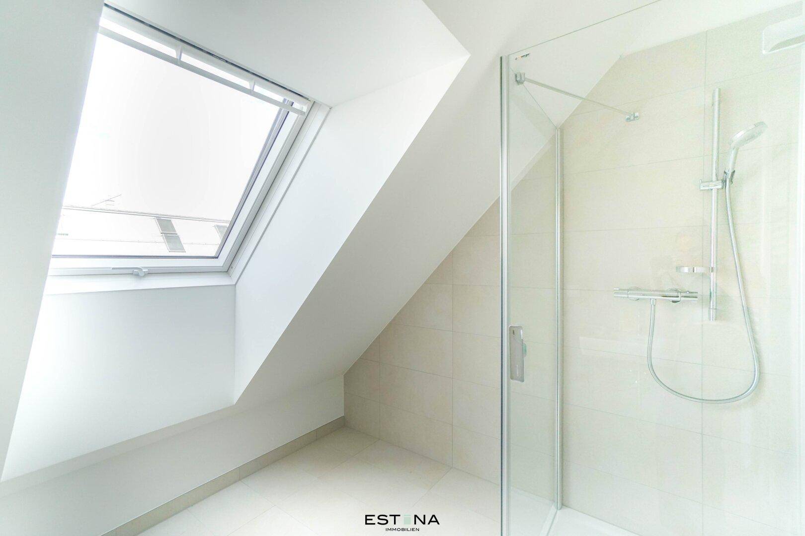 Helles Badezimmer mit Dusche, Dachschräge und einem Dachfenster für natürliches Licht.