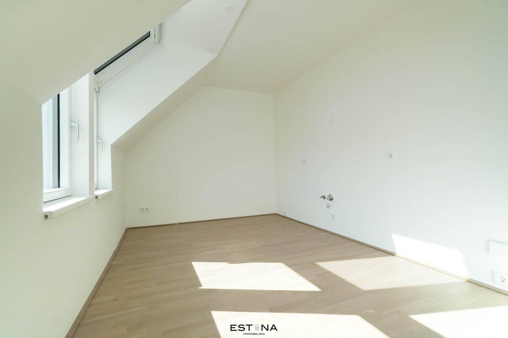 Unmöblierter Raum in Dachgeschosswohnung mit Holzboden, weißen Wänden und einem Dachfenster.