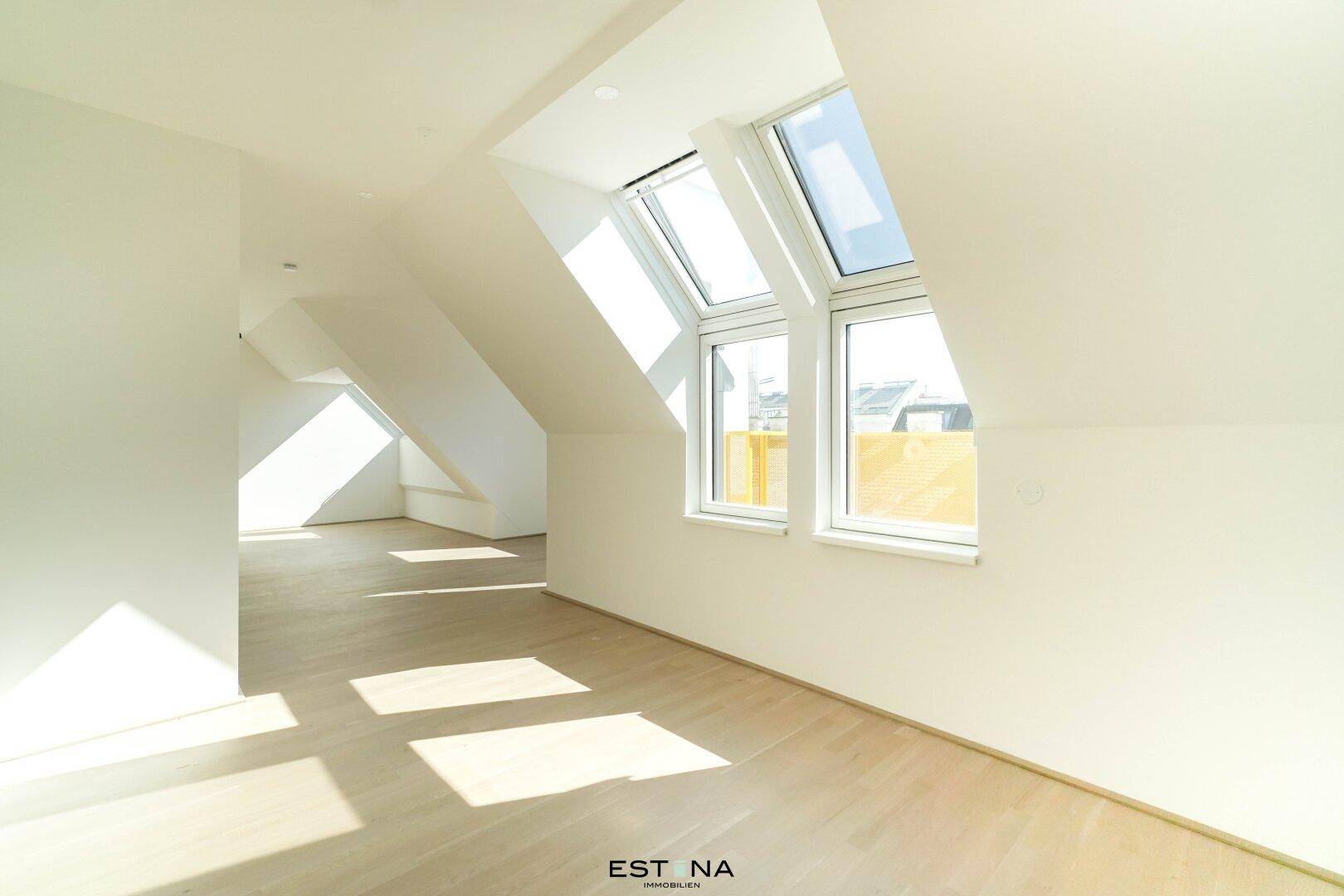 Lichtdurchfluteter Raum in Dachgeschosswohnung mit schrägen Wänden und hellen Holzfußböden.