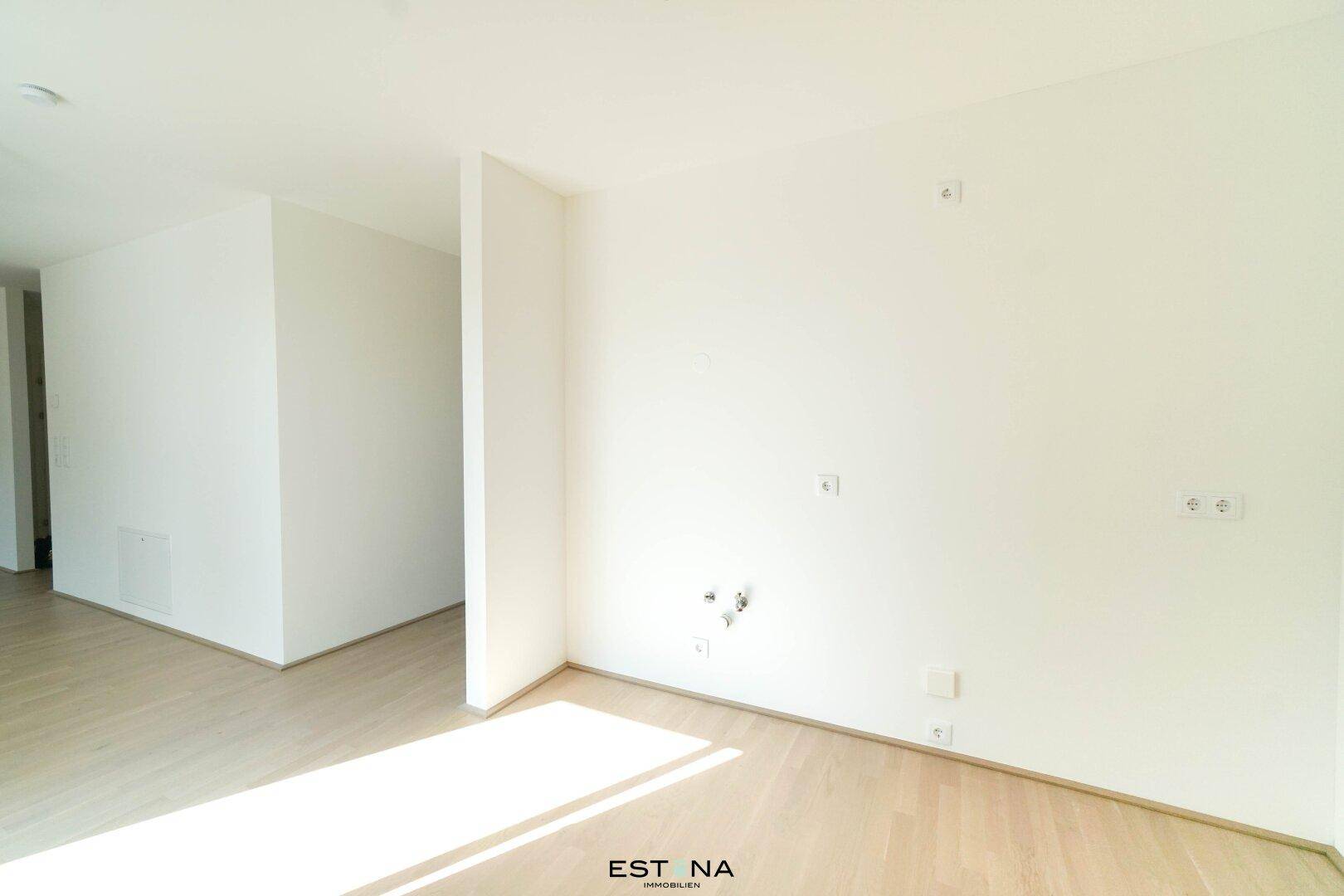 Leerer Raum mit Parkettboden und Anschlüssen an der Wand, bereit für die Installation einer Küche.