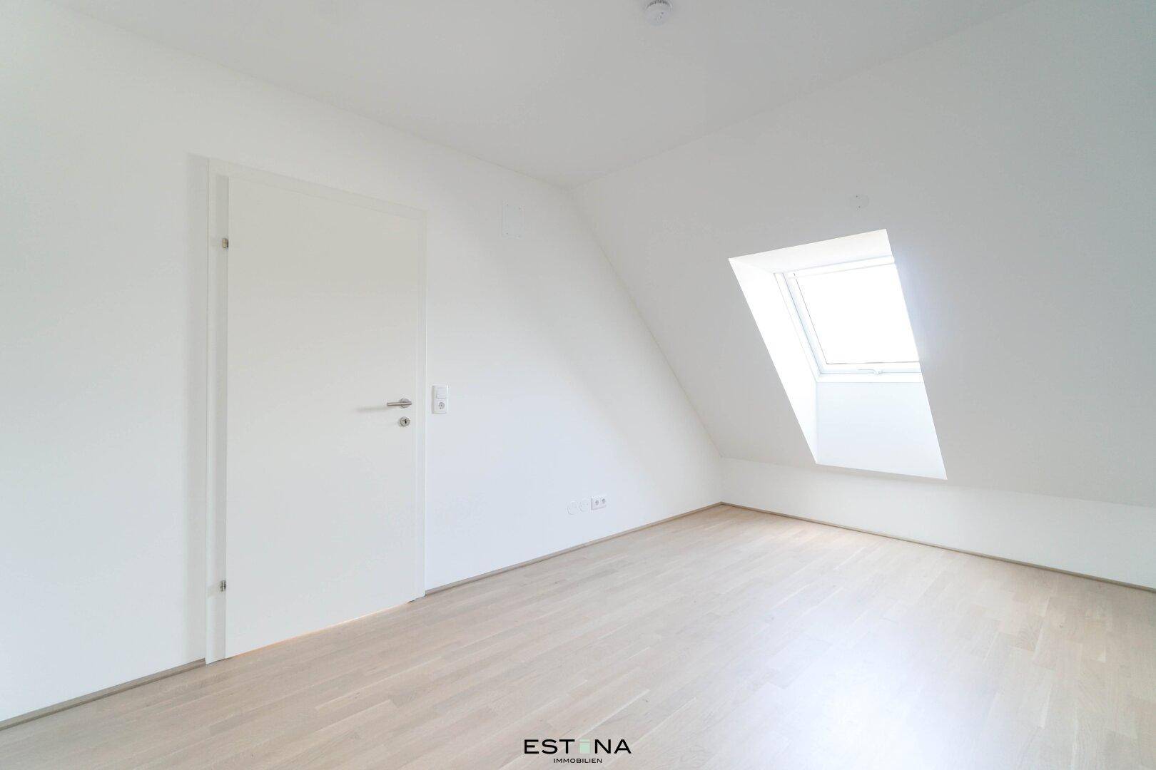 Helles Schlafzimmer im Dachgeschoss mit schrägen Wänden, Dachfenster und hellem Parkettboden.
