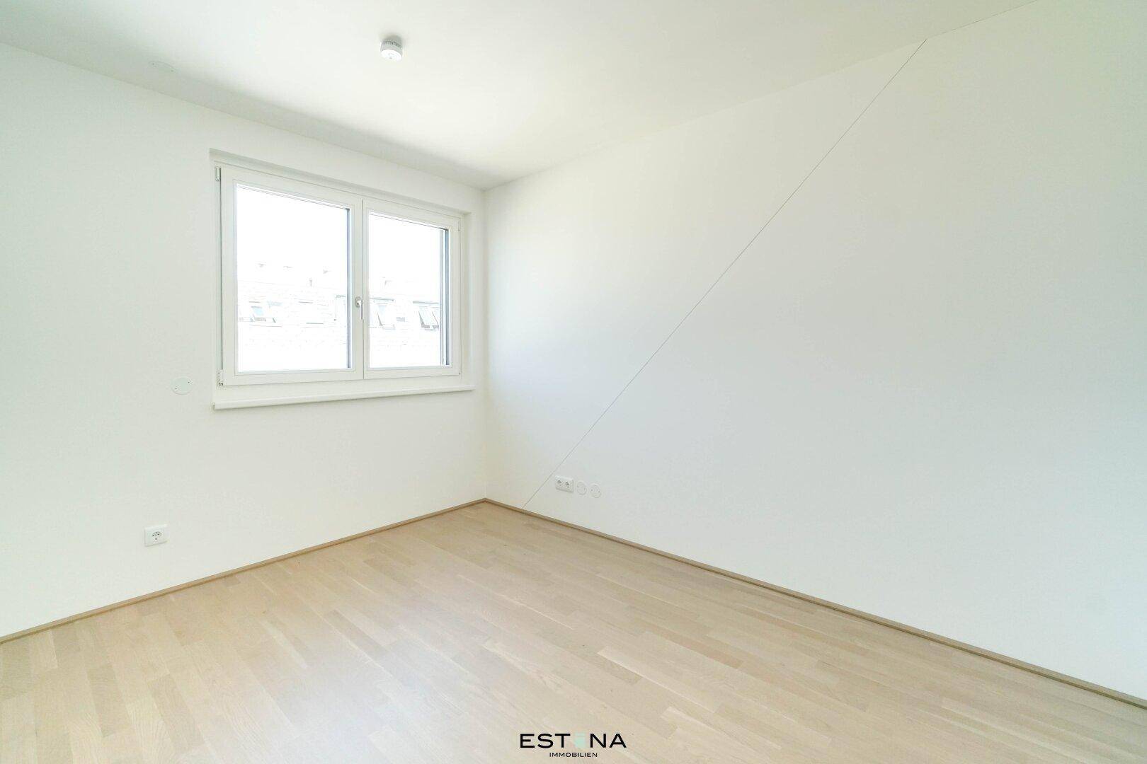 Helles Schlafzimmer mit Fenster und schräger Wand, ausgestattet mit modernem Parkettboden.