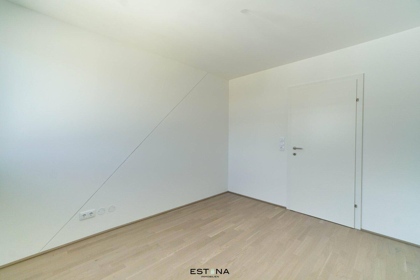 Geräumiges Schlafzimmer mit schräger Wand und hellem Parkettboden, bietet viel Platz für Möbel.