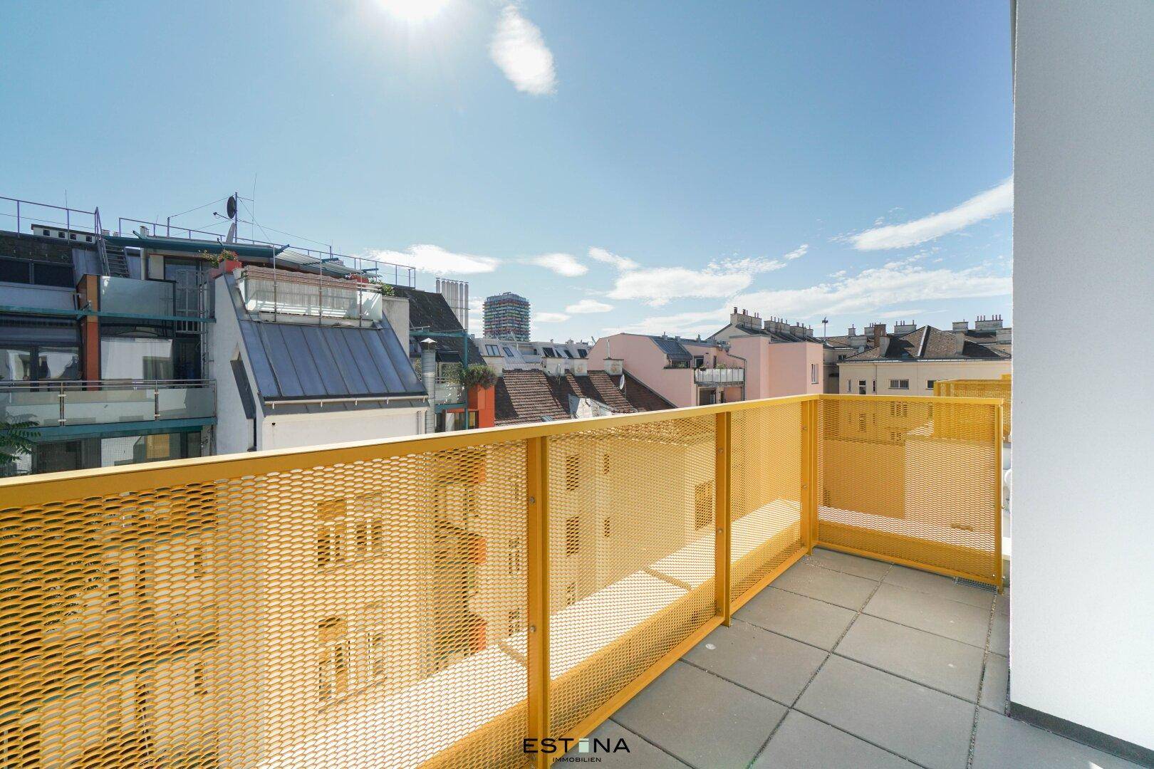Weitläufige Terrasse mit gelbem Gittergeländer und Blick auf die städtische Umgebung unter blauem Himmel.