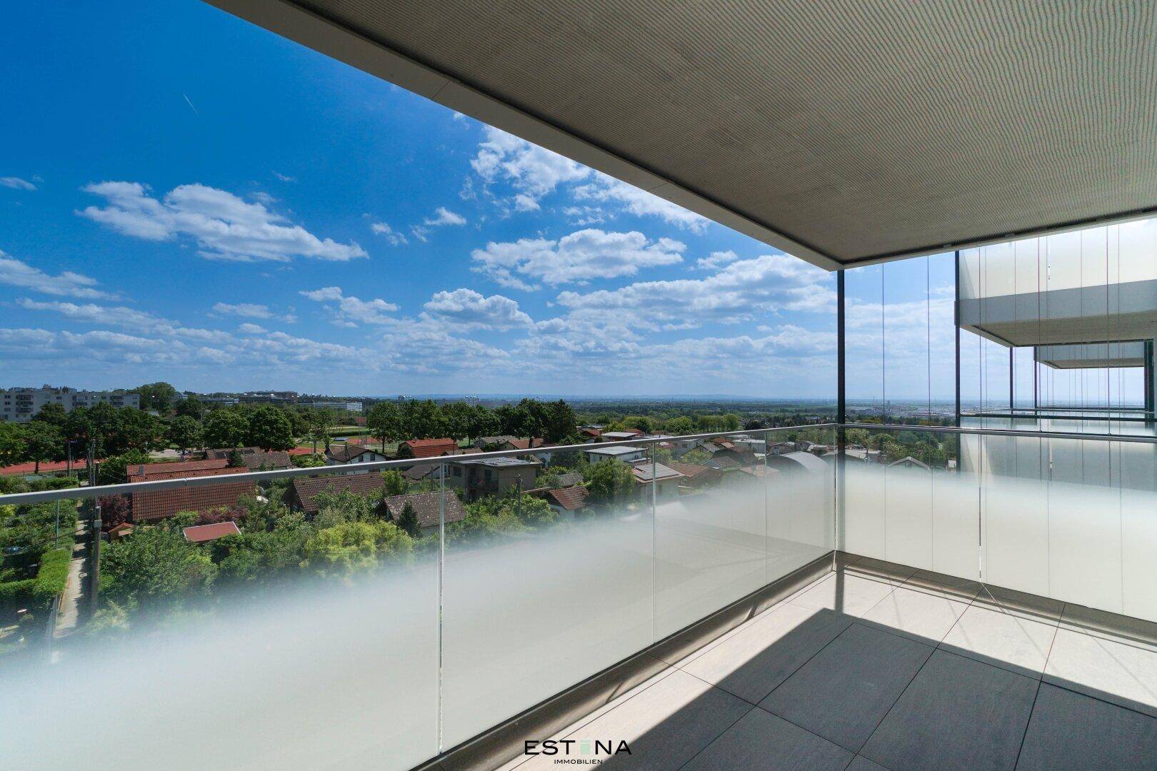 Geräumiger Balkon mit Glasgeländer und weitem Blick über die umliegende Wohngegend und Landschaft.