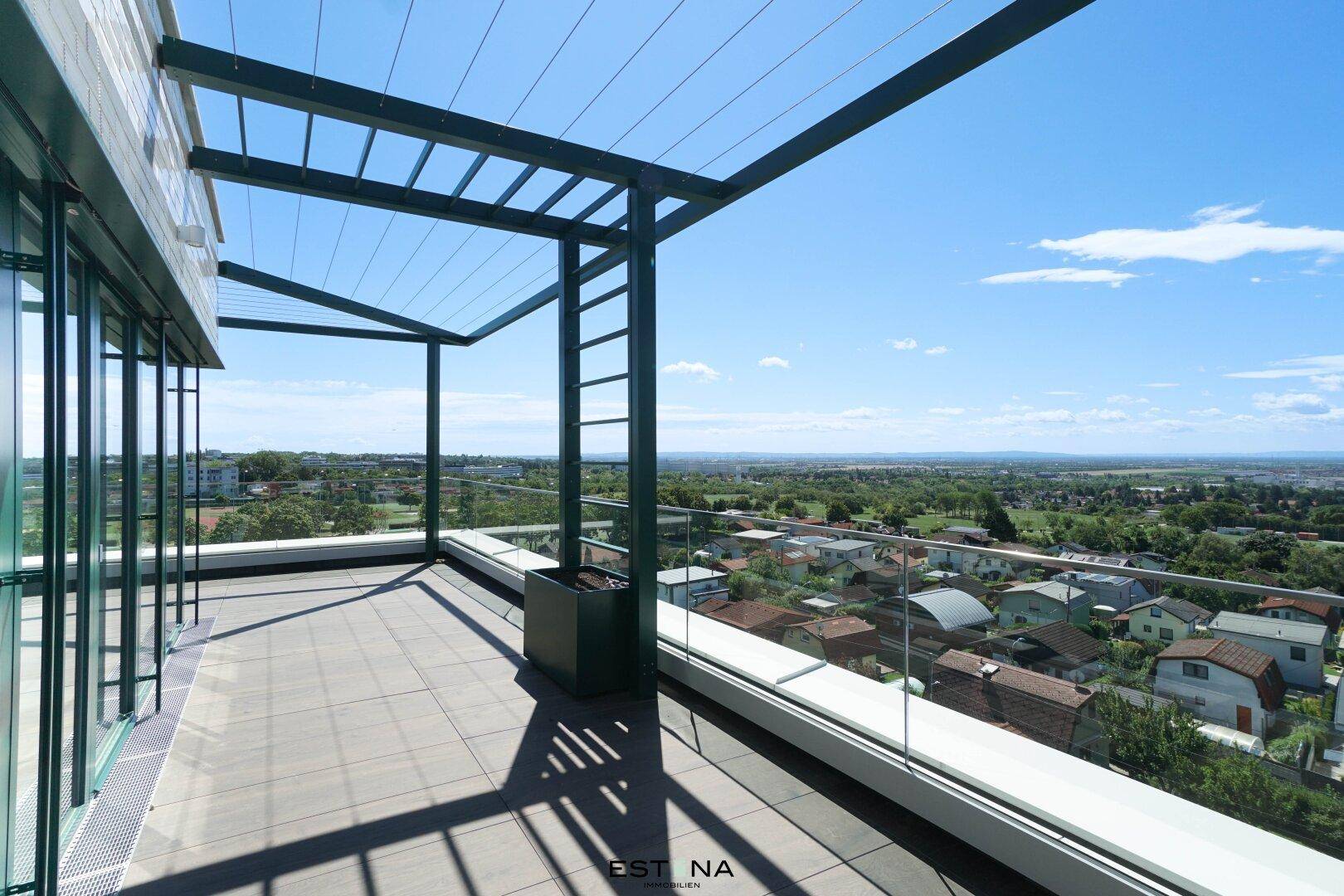Weitläufige Terrasse mit Fliesenboden, Glasgeländer und grüner Pergola, ideal für Entspannung im Freien.