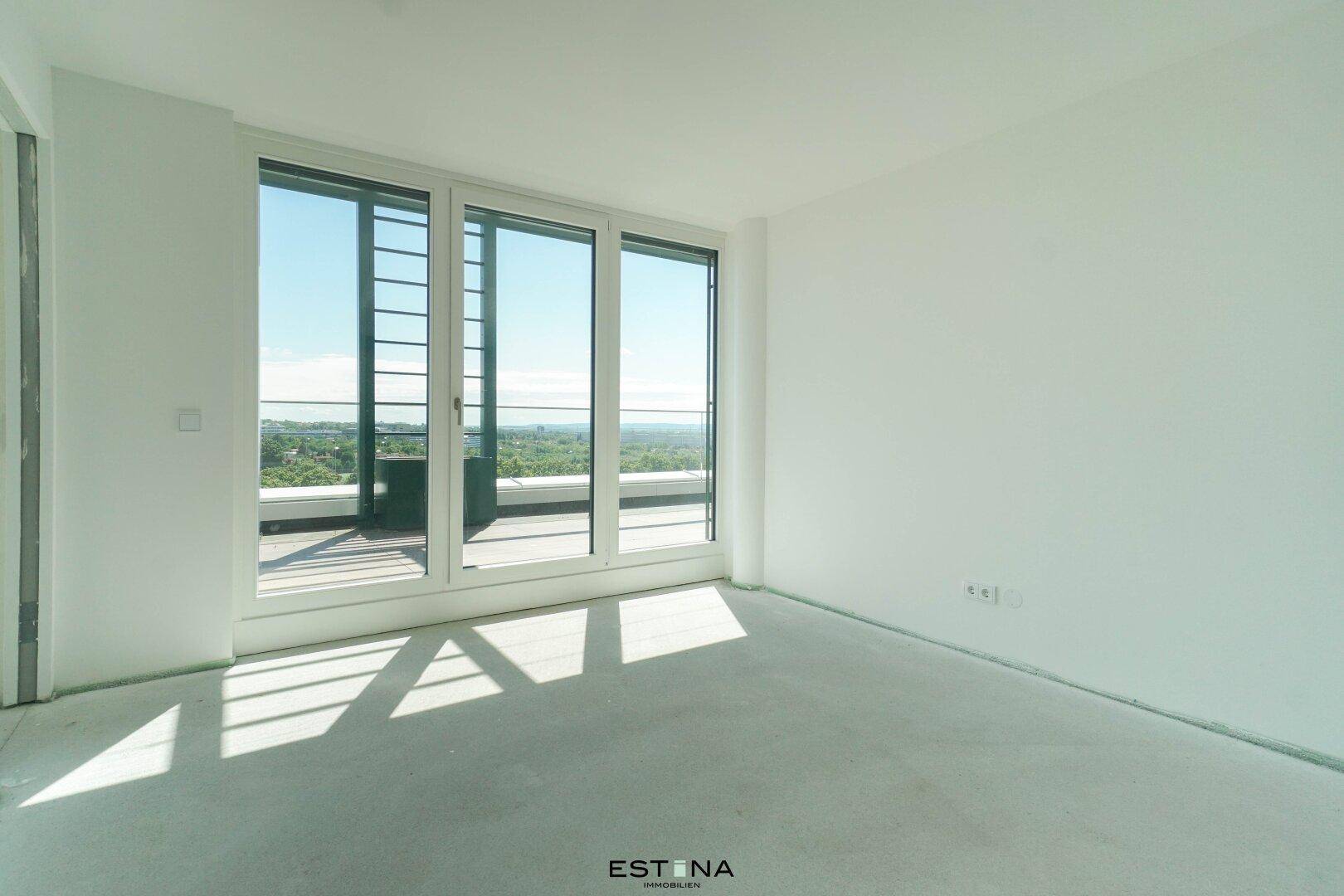 Helles, leeres Zimmer mit großem Fenster und Zugang zu einer Terrasse, bietet weite Aussicht.