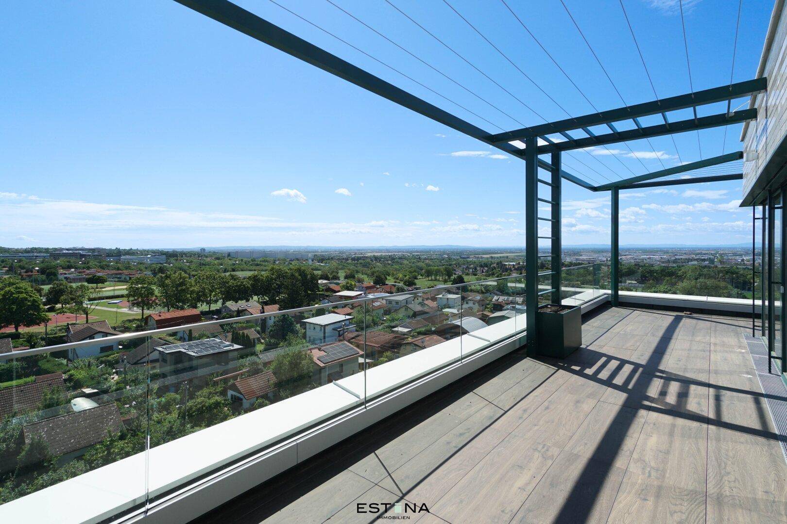 Geräumige Terrasse mit Holzoptikboden, Glasgeländer und Pergola, bietet einen weiten Ausblick.