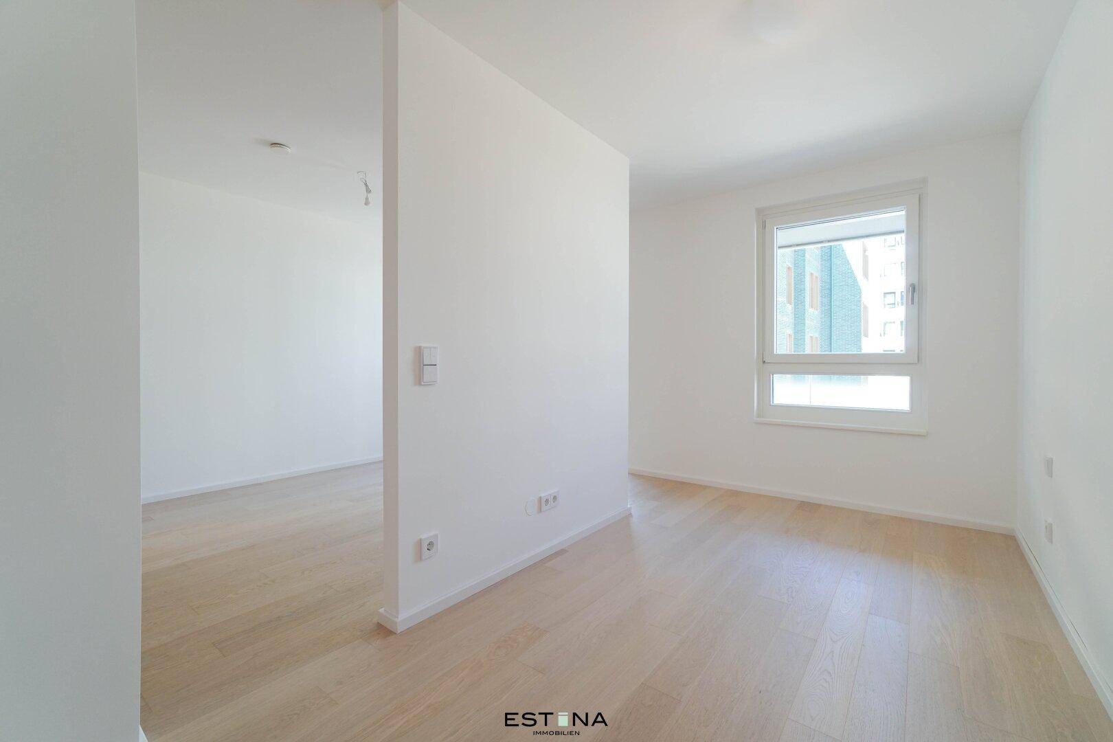 Geräumiges, helles Zimmer mit Parkettboden und einem großen Fenster, das viel Tageslicht hereinlässt.