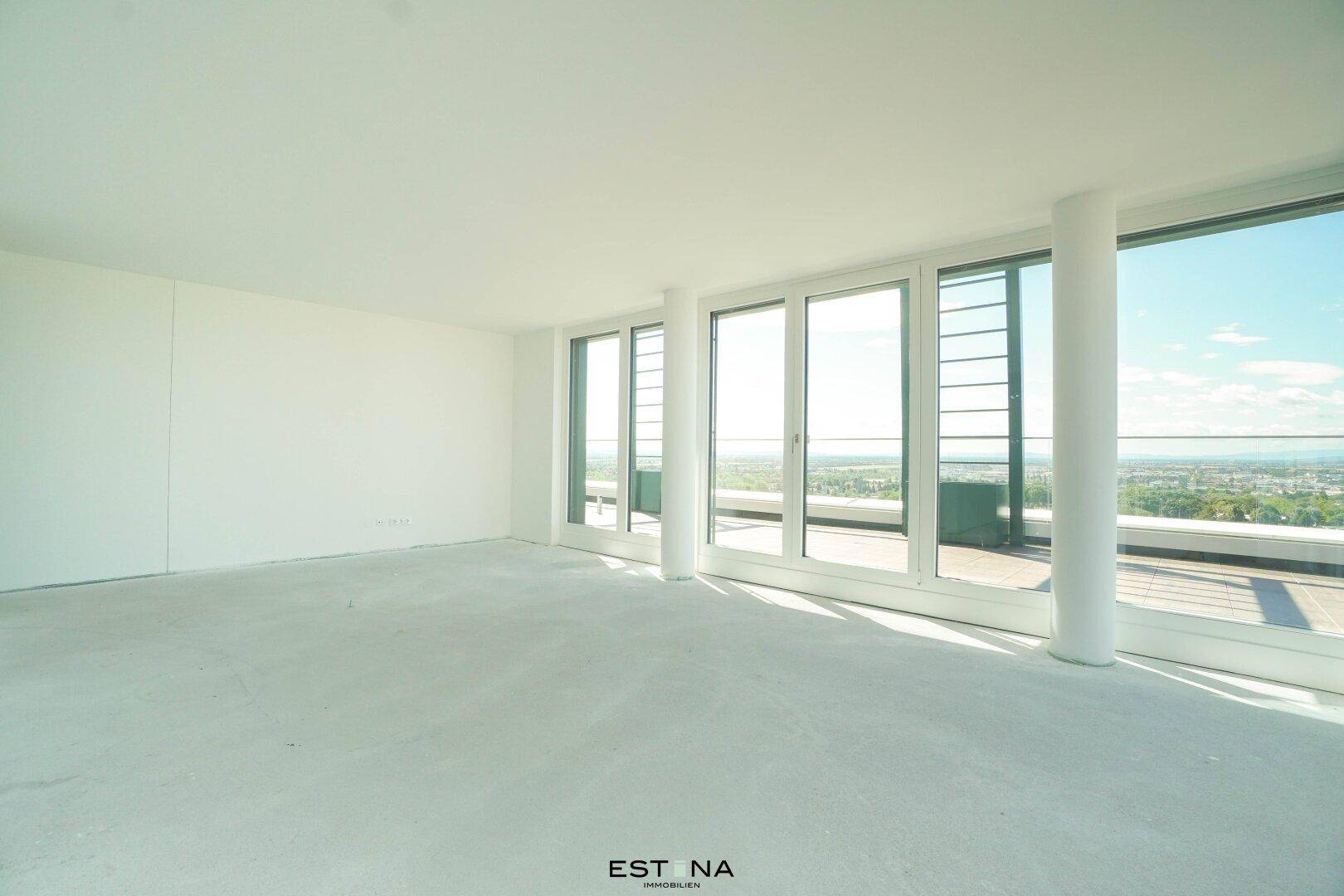 Geräumiger, heller Wohnbereich mit unverputzten Wänden und weitem Ausblick durch große Fenster.