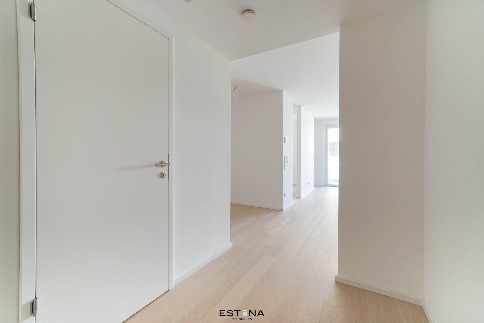Heller Flur mit weißer Tür und durchgehendem hellen Holzfußboden in einem modernen Gebäude.
