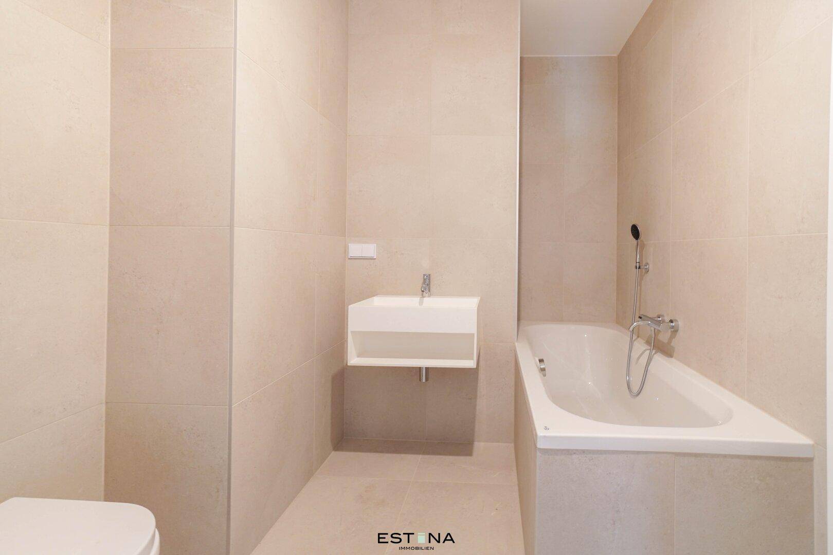 Modernes Badezimmer mit Badewanne, Waschbecken und hellen Fliesen in neutralen Farben.