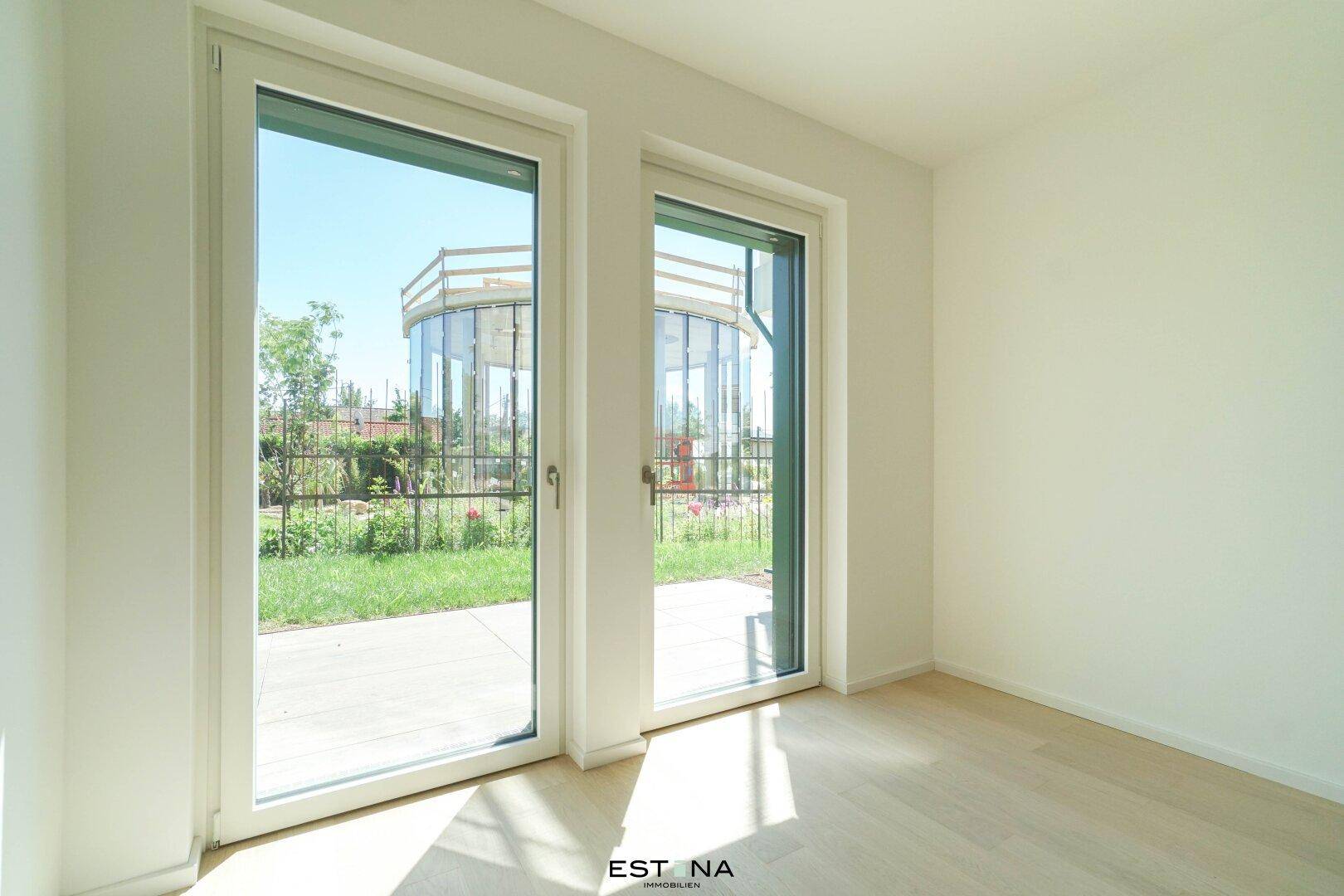 Helles Zimmer mit Parkettboden und großen Fenstertüren, die den Blick nach draußen freigeben.